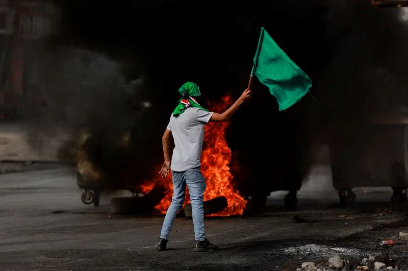 Seorang pria mengibarkan bendera selama bentrokan antara pasukan Israel dan Palestina, seiring berlanjutnya konflik antara Israel dan kelompok Islamis Palestina, Hamas, di dekat Ramallah, di Tepi Barat yang diduduki Israel, 27 Oktober 2023.